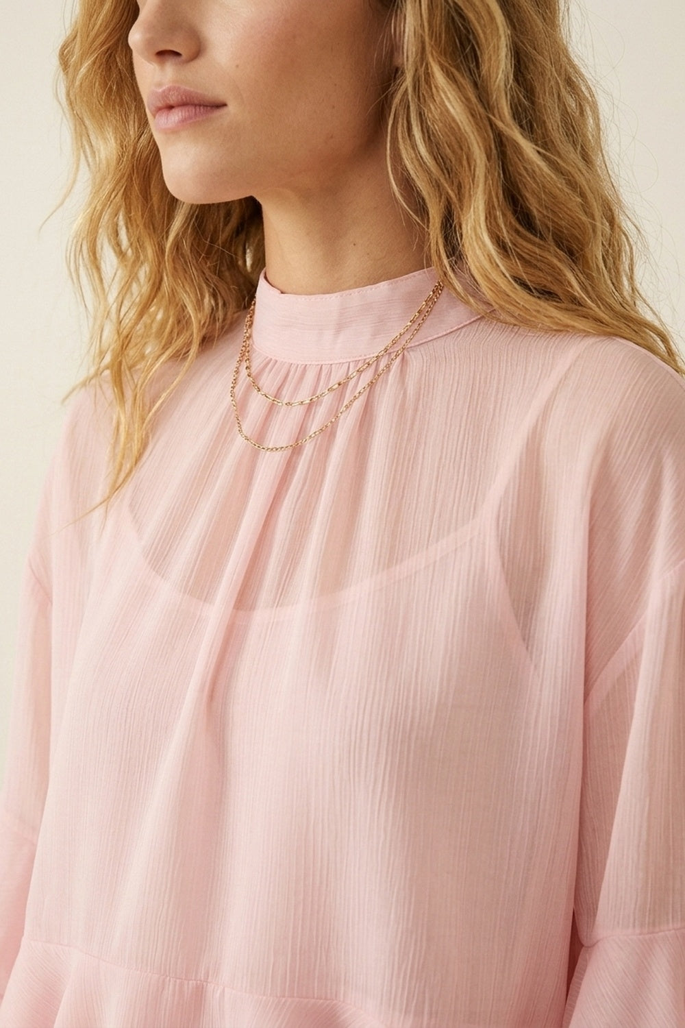 Blusa assimétrica de chiffon rosa claro com folhos em camadas e gola alta.